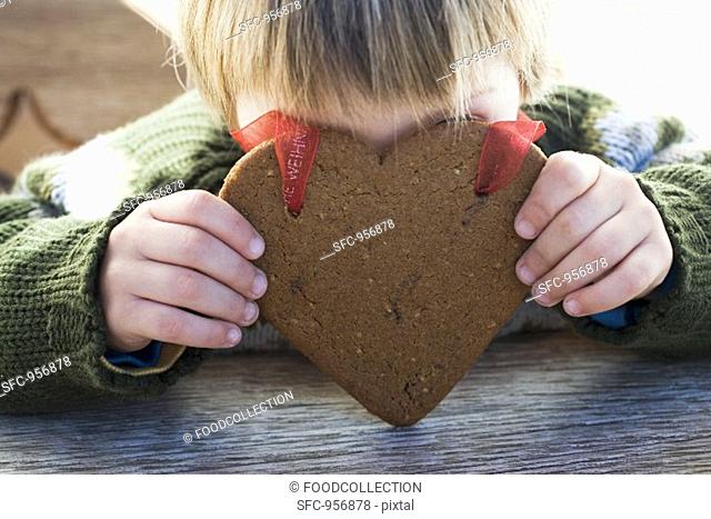Small boy holding gingerbread heart in front of his face