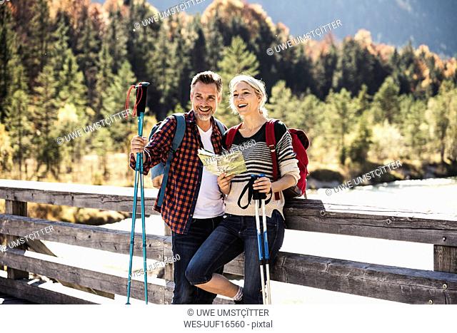 Austria, Alps, happy couple on a hiking trip with map on a bridge