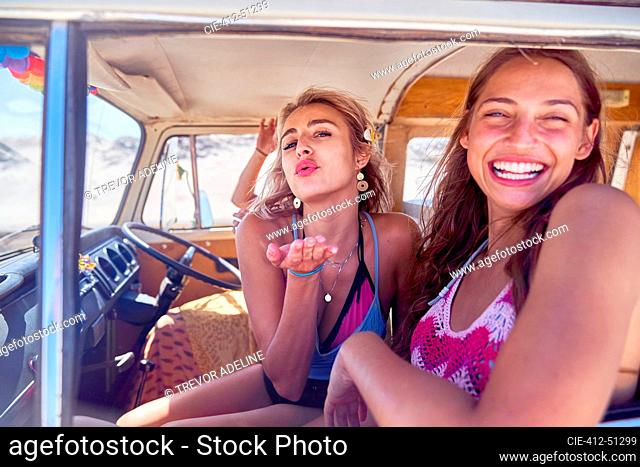 Portrait playful young women friends blowing a kiss inside van