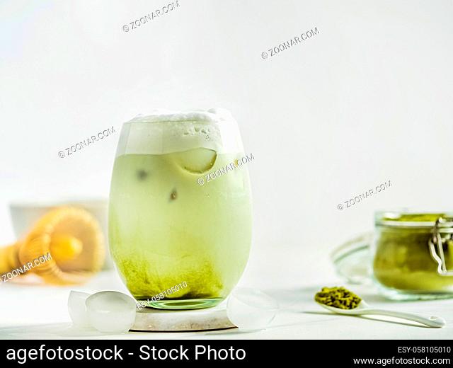 Iced Matcha Latte Tea with whipped cream in tumbler glass and ingredients on white marble background. Copy space for txt or design