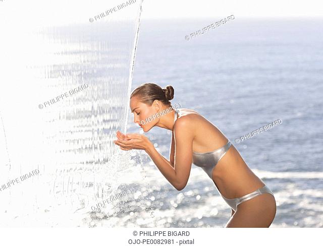 Woman in bathing suit standing under waterfall overlooking ocean