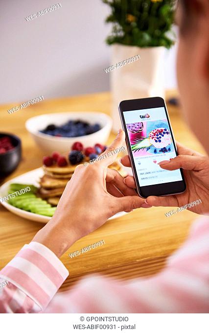 Young woman taking pictures of breakfast pancakes with berries and fresh fruit