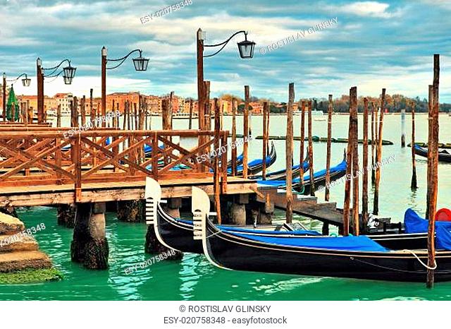 Gondolas moored in a row at wooden pier on Grand Canal in Venice, Italy