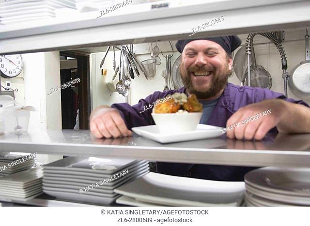 A fun caucasian bearded Chef dressed in purple laughing behind his window getting ready to serve vegan cauliflower. color, 30-40 caucasian male