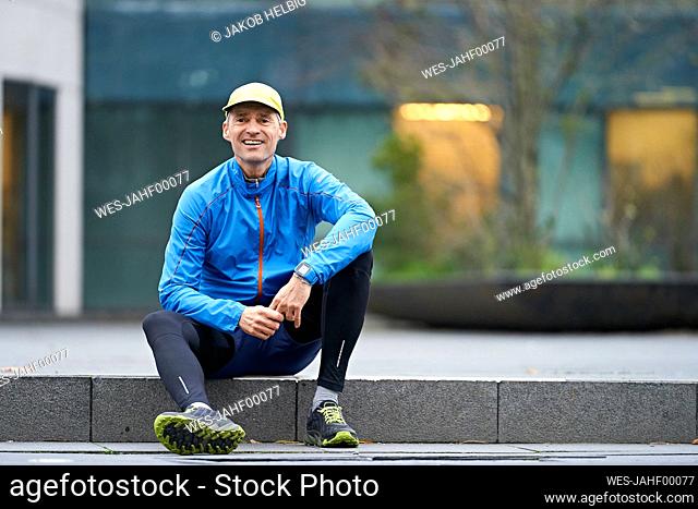 Smiling mature man wearing cap while sitting on pathway