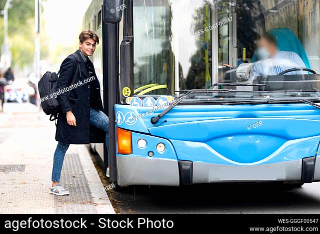 Smiling handsome young man with backpack boarding bus in city