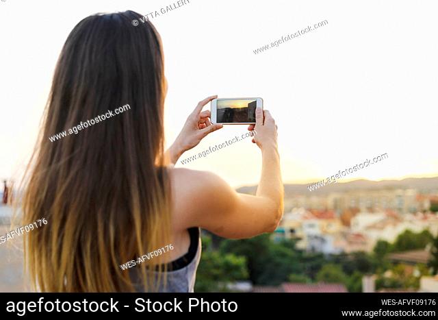 Woman photographing sunset view through smart phone at rooftop