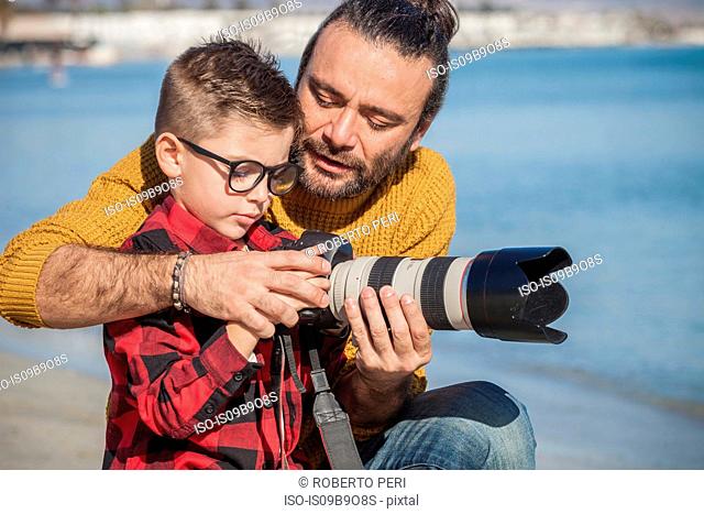 Father and son outdoors, father teaching son to use camera