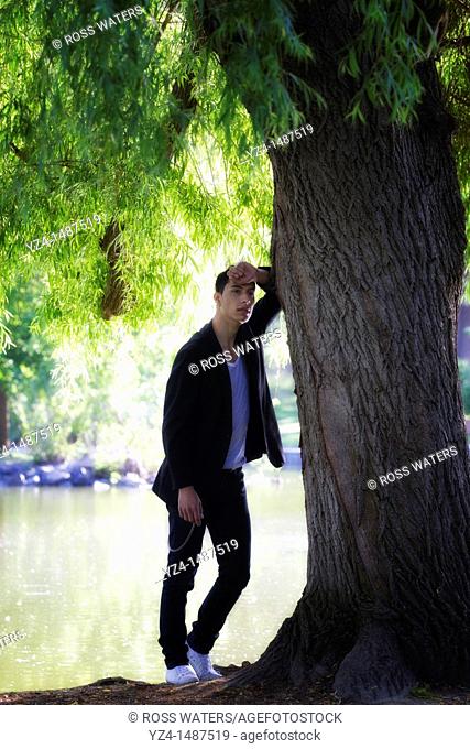 A young latino man leaning against a tree