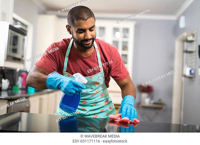 Young man cleaning marble counter in kitchen