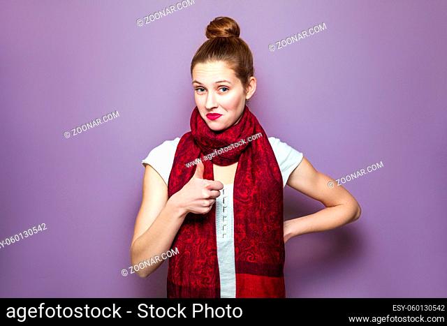 Thumbs up, young emotional girl with collected hair, freckles and red scarf looking excited with thumbs up on purple background