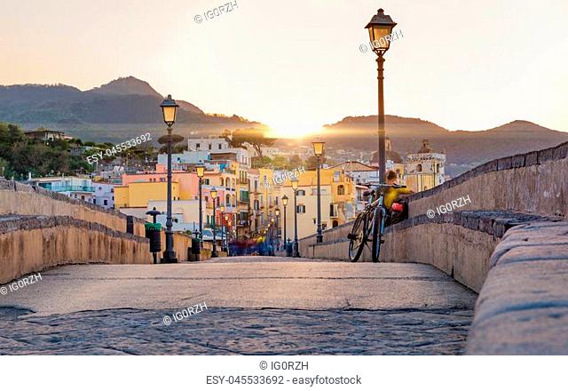 Sunset view from side of Aragonese Castle on Ischia street with colourful houses, Ischia Island, Italy. People blurred due to very long exposure time