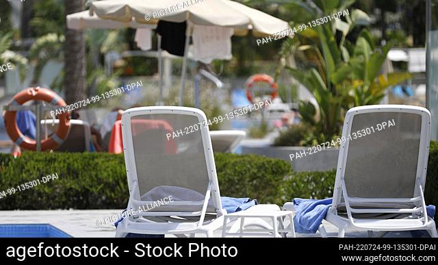 20 July 2022, Spain, Palma: Towels lying on sun loungers by a pool. Finally, vacation with beach and pool again. Hotels are full and with it