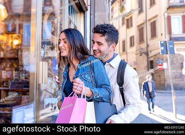 Smiling tourist couple window shopping while standing by store
