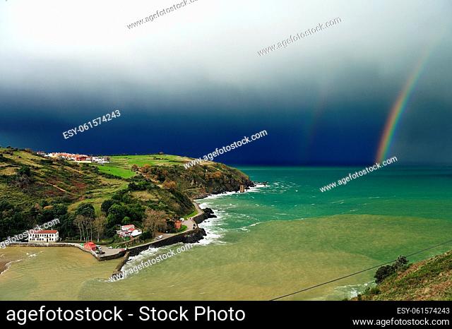 Cargadero de Mioño y playa de Dicido Cantabria con el arco iris de fondo, en un día de tormenta sobre un mar de color esmeralda
