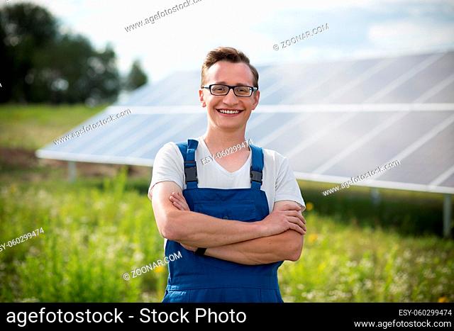 Worker standing in the field with solar with solar panels on backstage. Young man in glasses standing with his hands crossed