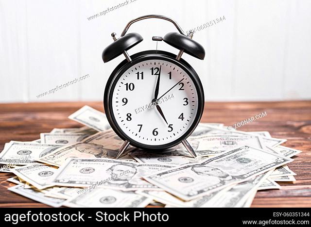 alarm clock on spread currency notes over wooden textured background