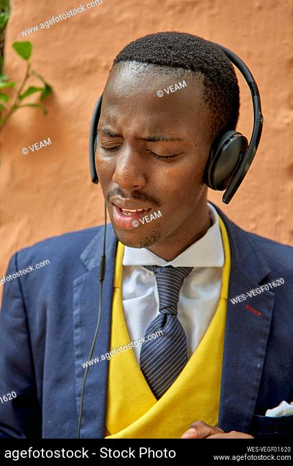 Stylish young businessman wearing old-fashioned suit listening to music on his headphones