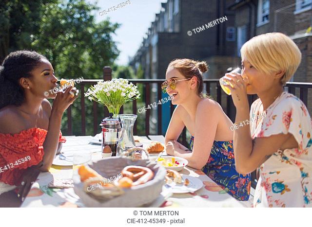Young women friends enjoying brunch on sunny apartment balcony