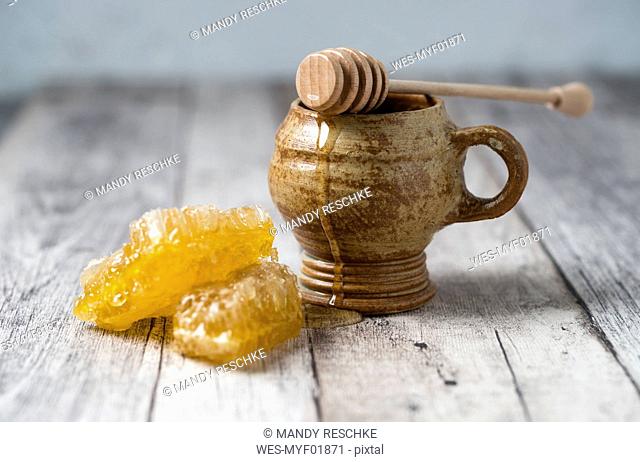 Honeycombs, clay pot and honey dipper on wood