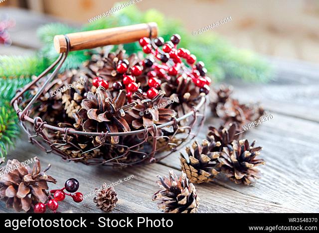 Christmas concept: full basket of pine cones and red holly berries and spruce branches on the background of old unpainted wooden boards