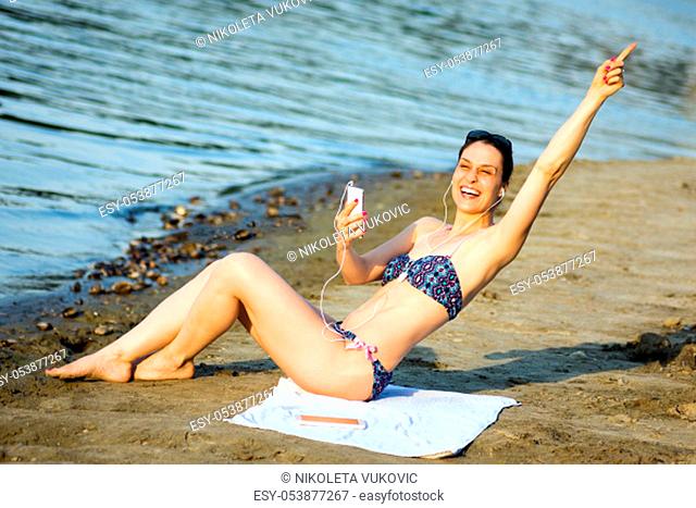 The attractive cheerful woman in bikini is having fun and using phone on the beach, summer lifestyle