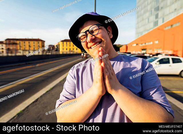 Smiling teenage boy with hands clasped on city street
