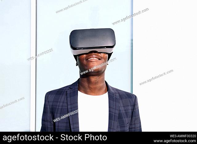 Smiling young man wearing VR glasses in front of wall