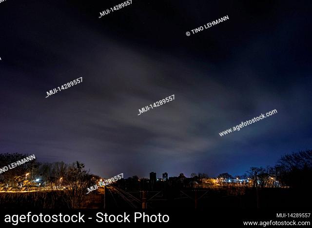 Long exposure at night with a view of the city of Luckenwalde, left a street, in the middle railway tracks, in the background large buildings