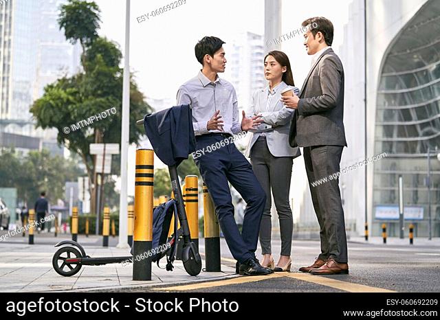 three asian business people chatting on street in downtown of modern city