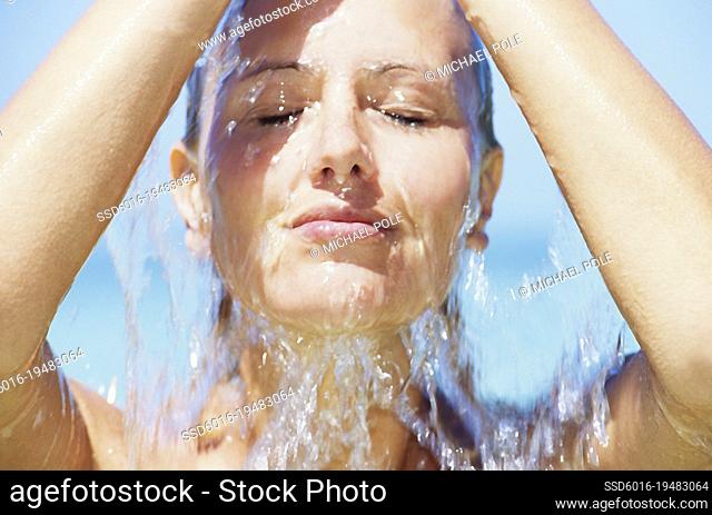 Close up of young woman splashing water down her face in tropical ocean