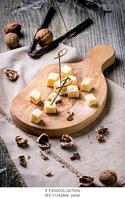 Small cubes of cheese on an olive wood chopping board with walnuts