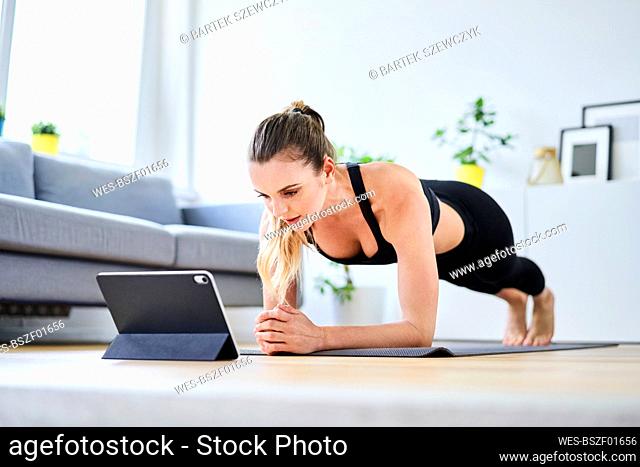 Woman learning plank exercise on internet through digital tablet at home