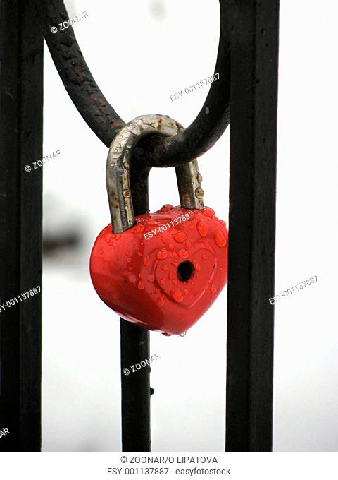 Red heart lock with the drops of rain. Metal fence