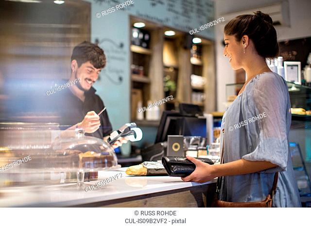 Barista calculating bill for female customer at cafe counter