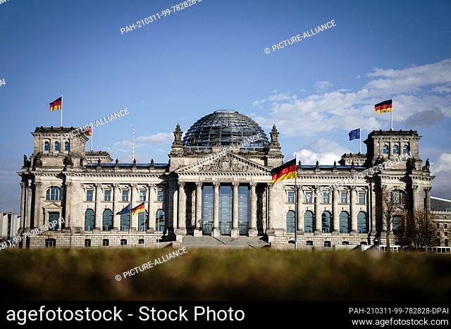 11 March 2021, Berlin: In the sunlight, the flags on the Reichstag building wave in the wind. Photo: Kay Nietfeld/dpa. - Berlin/Berlin/Germany