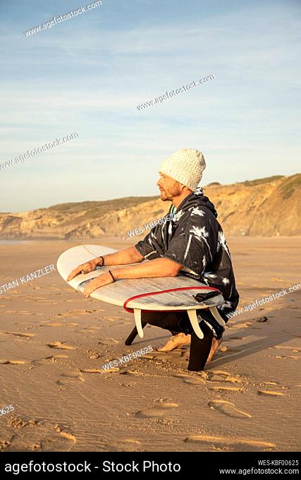 Male surfer looking away while crouching with surfboard at beach