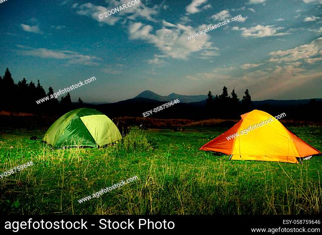 Twp illuminated camping tents on a field at night