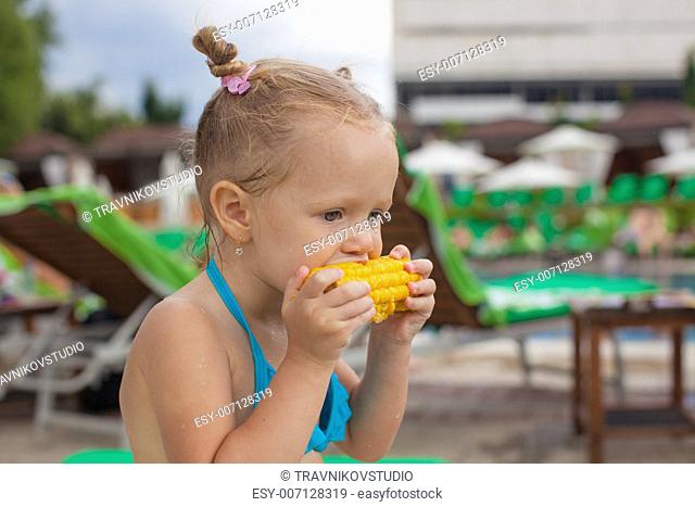 Cute little girl eating corn at the pool on vacation