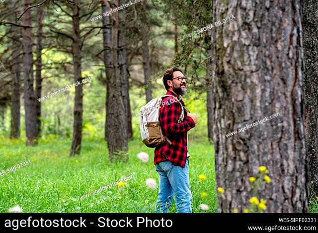 Smiling mature man with backpack walking in green forest
