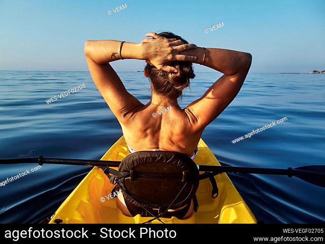 Woman with hands behind head sitting in boat against clear blue sky