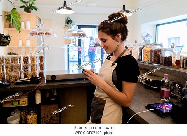Young woman using cell phone behind the counter in a cafe