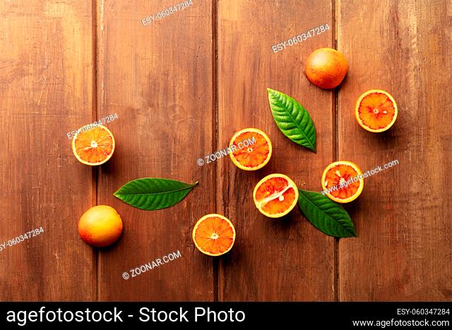 Organic blood oranges, shot from the top on a dark rustic wooden background with green leaves and a place for text