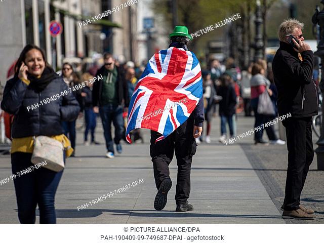 09 April 2019, Berlin: A man with a national flag of the United Kingdom on his back crosses a street in the city centre. Chancellor Merkel today received...