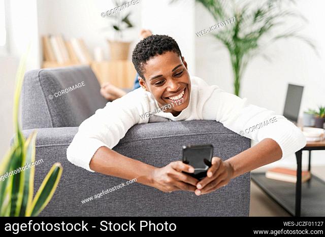 Smiling woman lying on couch using mobile phone