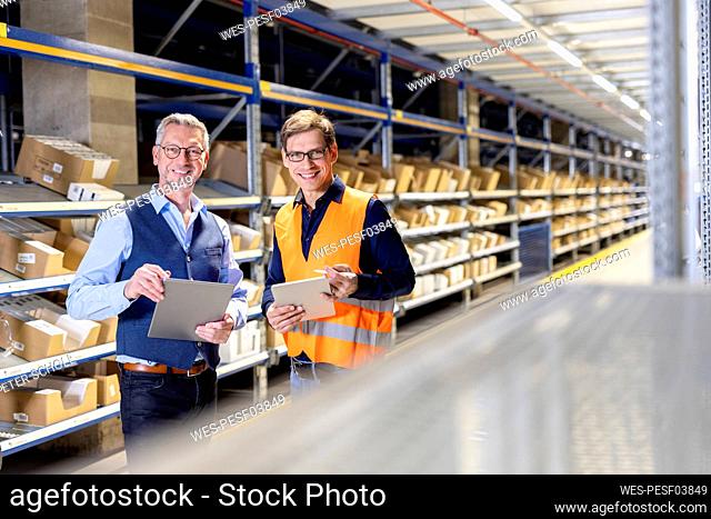 Smiling manager and worker with tablet PC standing in aisle at warehouse