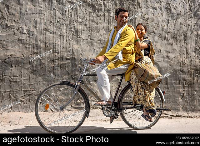 A HUSBAND RIDING A BICYCLE WITH WIFE SITTING BEHIND