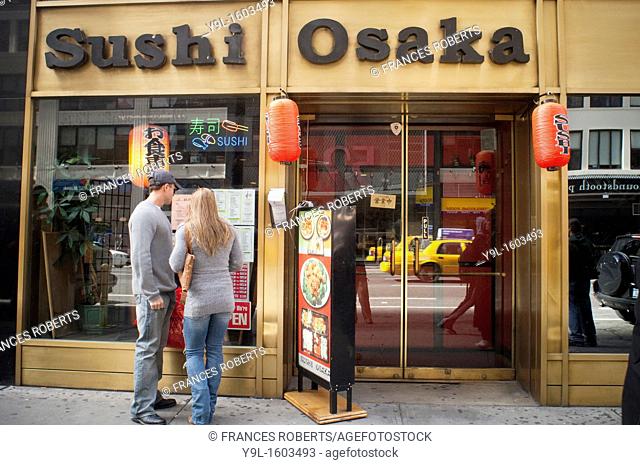 Passer-by read the menu in the window of Sushi Osaka, a Japanese restaurant, in midtown in New York