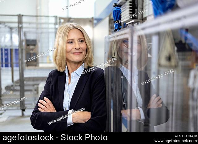 Smiling female professional with arms crossed standing by machinery in industry