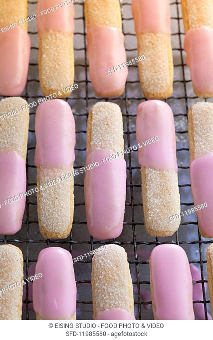 Sponge fingers with pink icing on a cake rack
